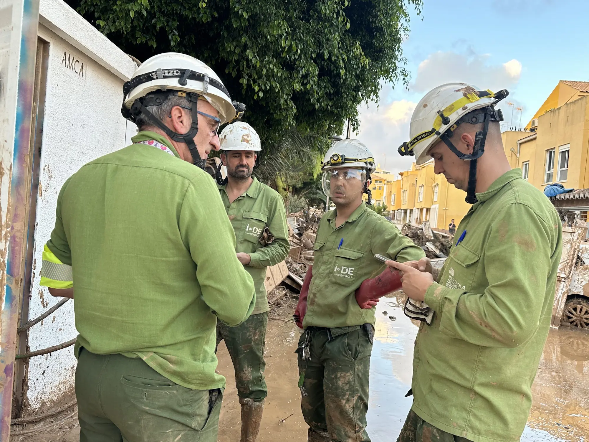 Cuatro trabajadores de Iberdrola con casco ayudando a establecer el suministro eléctrico “en tiempo récord” en las inundaciones de la DANA