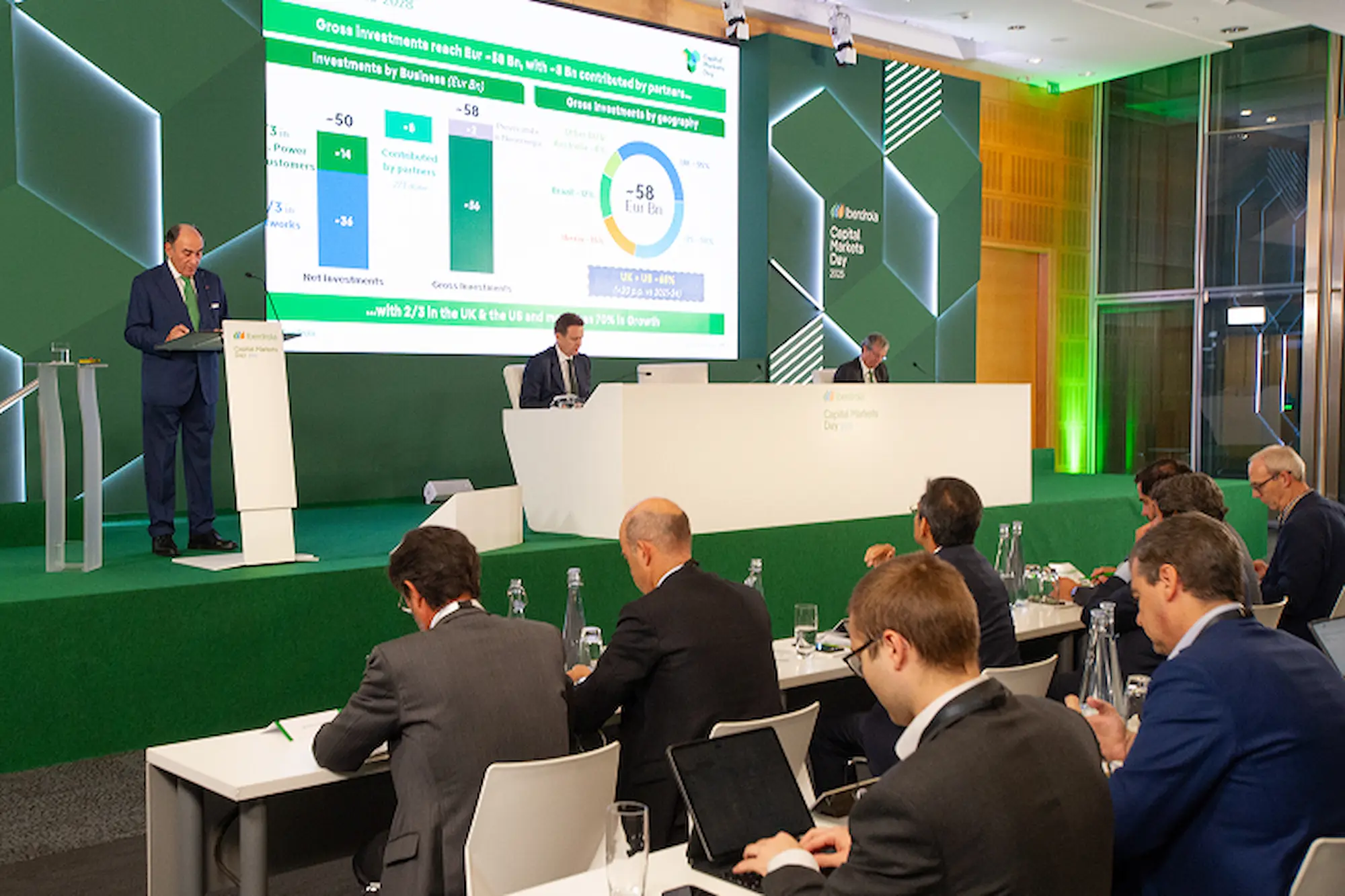 Imagen de una presentación en una sala de conferencias, con Ignacio S. Galán de pie frente a una pantalla que muestra gráficos, mientras varios asistentes se encuentran sentados, tomando notas.