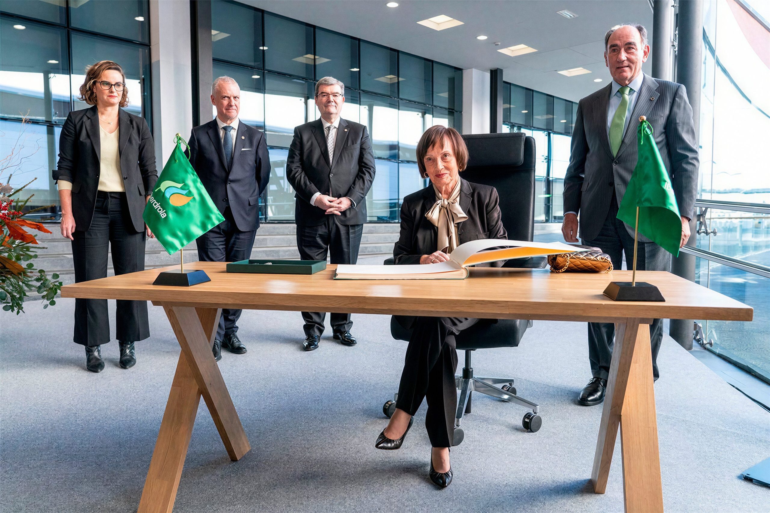Mujer sentada firmando un libro en una mesa, con varias personas de pie detrás en un entorno institucional de Iberdrola